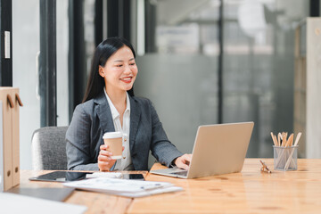 A professional woman working on laptop, smiling with coffee cup in hand
