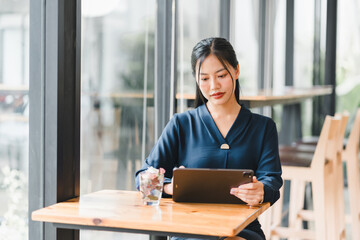 A woman in blue outfit is focused on her tablet in modern cafe