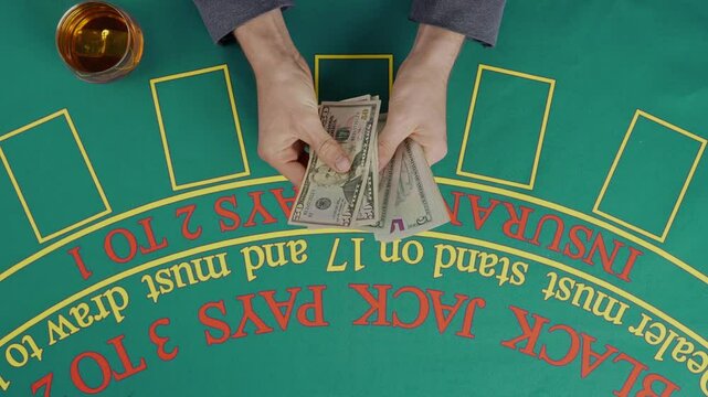 Gaming and casino payment concept. Top view of blackjack casino table, man player counting dollar banknotes and giving money to the croupier.