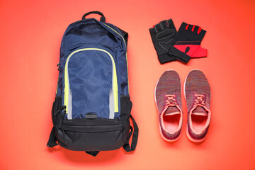 Fototapeta premium Backpack, fingerless cycling gloves and sneakers on coral background, flat lay