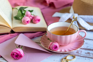 A cup of aromatic tea, a book and a rose on the table.