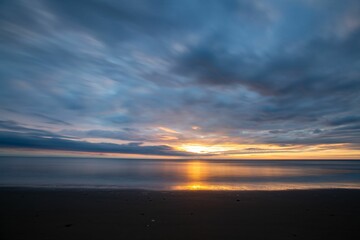 Sunset over calm ocean with cloudy sky