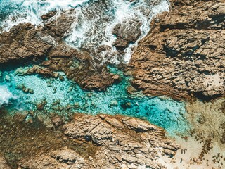 Aerial view of a rocky coastline with turquoise waters and waves crashing against the rocks.