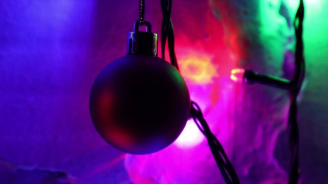Una toma de cerca de una bola de navidad guindada en varias luces de colores en una pared de color blanco. Decoraci&oacute;n de navidad y fin de a&ntilde;o