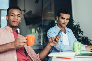 Portrait of millennial employees in casual wear sitting in coworking space near table desktop and posing during time for together brainstorming, diversity executive marketers looking at camera