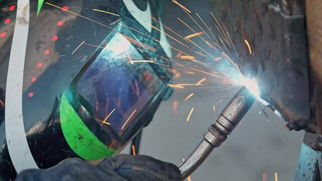 A close-up image of the welding process, with bright sparks lighting up the scene as a person uses protective gear to weld metal pieces together in a controlled workshop environment.