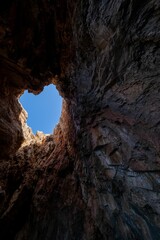 Low angle vertical shot of a cave opening with a view of the blue sky above in Zakynthos, Greece
