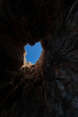 Vertical low angle view of a cave opening with a view of the blue sky above in Zakynthos, Greece