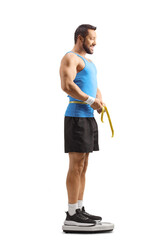 Fit man in sportswear measuring waist and standing on a weight scale