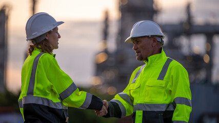 Engineer industry jackets and hard hats standing in an industrial area,  refinery or power plant. They posing hand shake in a safety drill or  gesture of acknowledgment is teamwork industry concept.