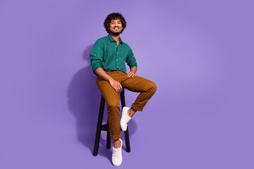 Full body length photo of handsome hispanic guy in bar sitting comfortable stool carefree relaxing isolated on violet color background