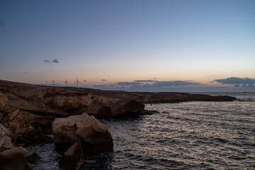 The sky is a beautiful shade of pink and orange as the sun sets. The water is calm and the rocks are jagged © AlbertoRodriguez