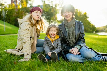 Two big sisters and their toddler brother having fun outdoors. Two young girls with a toddler boy on autumn day.