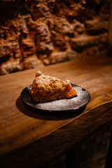 A piece of mango cake on a wooden background. Delicious pie with fruit and powdered sugar on the table side view