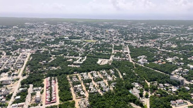 aerial drone view of downtown tulum with buildings and houses surrounded by green tropical areas and Caribbean Sea on the background on a cloudy morning in Mexico