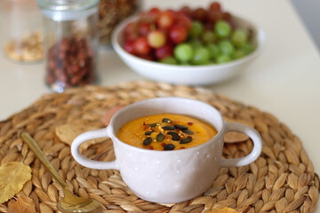 Pumpkin and potato creamy soup, bowl of grapes, jars of nuts and autumn leaves on the table. Selective focus. 