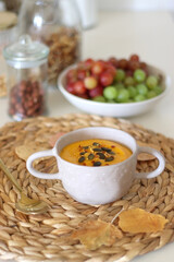 Pumpkin and potato creamy soup, bowl of grapes, jars of nuts and autumn leaves on the table. Selective focus. 