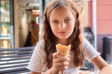 Brown haired Caucasian schoolgirl eating delicious ice cream outdoors holding waffle cone filled with tasty ice cream enjoying her day outdoors during summer holiday