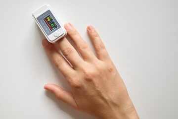 Unrecognizable woman having her blood oxygen level and heart rate measured by digital oximeter on her fingertip during health checkup with modern medical technology