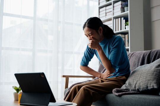 Woman in the living room at home has stomach ache and press hands to stomach due to menstrual cramps period cramps splenomegaly  food poisoning excess gas or acid and vomit
