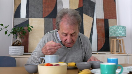 Elderly man eating breakfast at the table, highlighting a calm morning routine and a moment of quiet reflection in a cozy, domestic setting