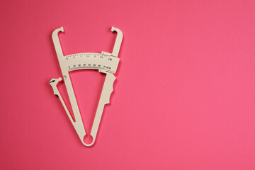 Plastic body fat caliper on pink background, top view. Space for text