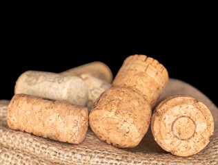 Several wine corks on a jute bag, macro, isolated on black background.