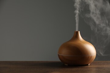 Aroma oil diffuser with steam on wooden table, space for text