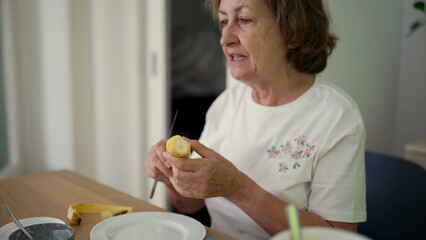 Elderly woman peeling a banana at the table, illustrating a simple and peaceful moment of daily life in a cozy home environment
