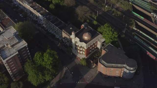 Aerial tilting down over Finsbury Park mosque with railway and tower blocks in the background and Londoners roaming in the streets