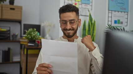 Young hispanic man in an office celebrates a positive achievement while reading a document with excitement and joy.
