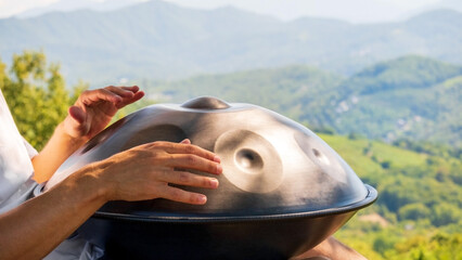 Close-up male hands playing a handpanon the background of mountains