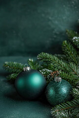 Two green Christmas ornaments resting on pine branches against a dark green background, creating an elegant and festive scene.