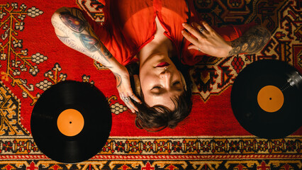 Top view woman lying down on red carpet  and listening old vinyl records.