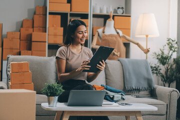 Asian SME business women use laptop computer checking customer order online shipping boxes at home....