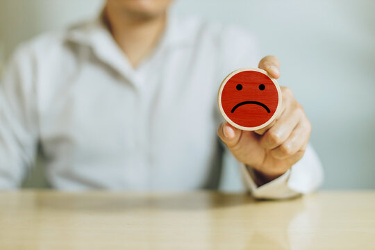 Service rating, satisfaction and negative feedback. A man hold wooden cube with bad face emoticon give a one star rating indicates the lowest level of satisfaction with the service