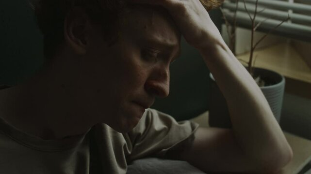 Close-up view of young man touching forehead and ginger hair experiencing panic attack at home