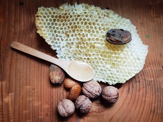 Honey in honeycomb with wooden spoon, almonds and walnuts in shell