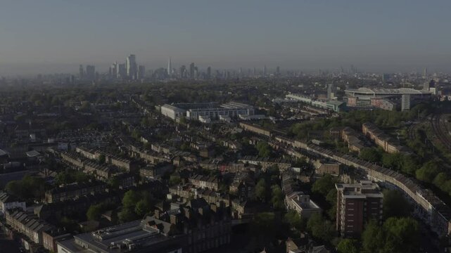 Wide aerial moving forwards of North London with railway on the far left and residential houses and Arsnenal Emirates Stadium in the foreground and sky scrapers in the background