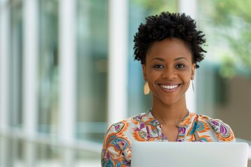 Portrait of a confident woman with an afro puff hairstyle, wearing glasses and large hoop earrings, working on a laptop in a vibrant yellow and green outfit.