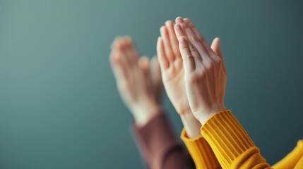 Close-up of multiple hands clapping in applause during an event, with a focus on two individuals wearing yellow and brown sleeves, set against a neutral background.
