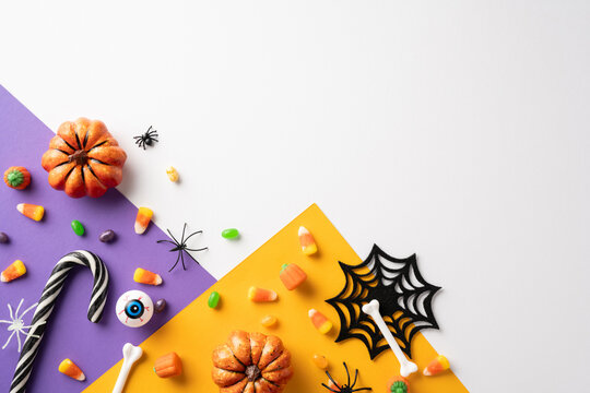 Creative Halloween setup featuring candy corn, mini pumpkins, spiders, and bone decorations on a vibrant purple and orange background