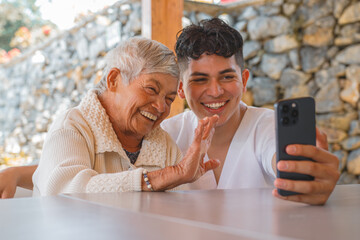 Elderly woman and caregiver smiling and waving during a video call, expressing connection and joy through modern technology, showing intergenerational bond and communication