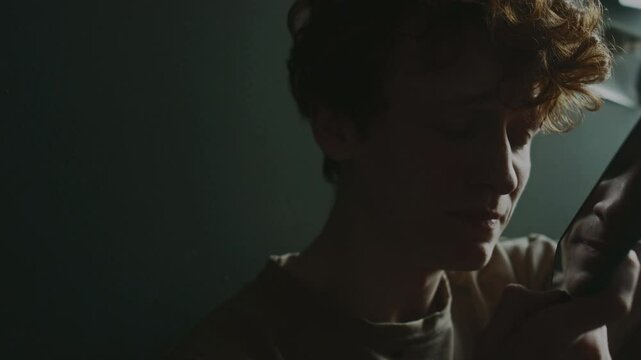 Close-up view of anxious young man recording voice message holding smartphone in front of himself in his room