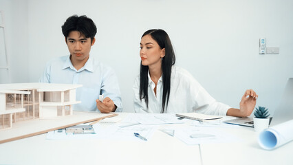 Professional male engineer measure house model by using ruler while beautiful cooperative coworker working together by using laptop to analysis data. Creative design and teamwork. Closeup. Immaculate.