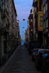 Fototapeta premium Street in a city with parked cars on both sides leading to a view of the Basfor and ships