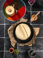 View of traditional Mexican tortillas on a black plate with various kitchen items on a tiled surface