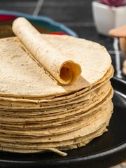 Close-up of a stack of fresh corn tortillas with one rolled tortilla on top, set on a black plate