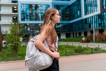 Portrait of a beautiful Caucasian girl with a backpack on the background of a high-rise building. A high school student goes to school.