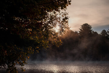 Morning fog on the lake in the autumn. The sun rises over the lake. Algonquin Park, Ontario, Canada. 
